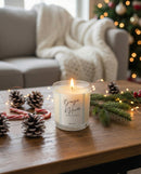 Bougie d’Hiver artisanale Sakura en cire de soja, allumée sur une table en bois dans une ambiance de Noël avec pommes de pin, branche de sapin et guirlandes lumineuses – fabrication suisse.