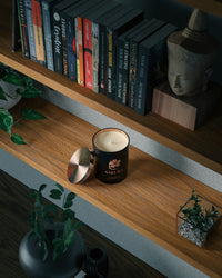 Bougie parfumée artisanale suisse Sakura posée sur une étagère en bois dans une bibliothèque moderne, avec des livres et des éléments décoratifs – fabrication suisse en cire naturelle.