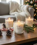 Trois bougies d’Hiver artisanales suisses Sakura allumées sur une table en bois, entourées de décorations de Noël comme des pommes de pin, branches de sapin et guirlandes lumineuses, créant une ambiance hivernale cosy.