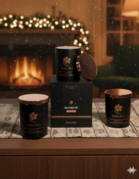 Trois bougies parfumées artisanales suisses Sakura édition Ikigai posées sur un meuble en bois avec leur coffret luxueux, devant une cheminée allumée et des décorations de Noël floues en arrière-plan – ambiance chaleureuse et festive.